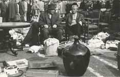 860518 Afbeelding van twee verkopers zittend bij hun handel op een rommelmarkt in Wijk C, neergezet op een van de vele ...